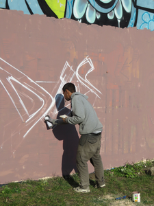 847117 Afbeelding van een graffitikunstenaar die een nieuw werk aan het opzetten is op een muur bij de tijdelijke ...